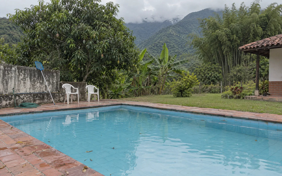 Piscina de una finca de clima cálido con montañas verdes y nubes bajas al fondo
